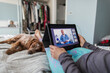 © Paul Bradbury/Caia Image - Woman with digital tablet video chatting with doctor on bed with dog
