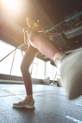 Bottom view of athletic woman in sportswear kicking with the leg while working out at industrial gym, warming up before training