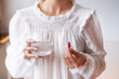 © Karyna - Woman in white blouse holding in hand iron Ferrum supplement capsule and glass of water. Bioactive additive woman pharmacy. Vitamin mineral treatment against anemia. Autumn health care concept