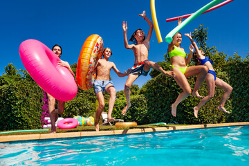 Group of teenage children have fun in the swimming pool diving with inflatable toys doughnuts jump and splash in the water