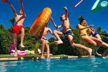 Wall Mural - Group of happy teen kids jump and dive in water throwing inflatable toys in the air splashing into the swimming pool