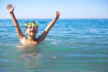 A boy with scuba diving glasses in the sea enjoys the summer sun, vacation and fun swimming