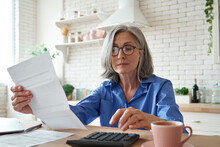 Senior Mature Business Woman Holding Paper Bill Using Calculator, Old Lady Managing Account Finance, Calculating Money Budget Tax, Planning Banking Loan Debt Pension Payment Sit At Home Kitchen Table.