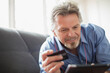 © Tom Merton/Caia Image - Senior man with headphones and credit card using digital tablet on sofa