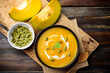 Pumpkin soup in a bowl and pumpkin seeds on wooden table, Top view