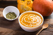 Pumpkin soup in a bowl with seeds and fresh pumpkin on wooden background
