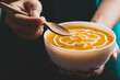 Pumpkin soup in a bowl holding by hand and eating