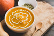 Pumpkin soup in a bowl with seeds and fresh pumpkin on wooden background