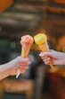 Close-up shot of two-hand holding a white and green ice cream cones. There is a blurred background of the shop and bokeh of the daytime light. Feeling fun and happy. Idea for dessert with copy space.