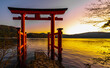 The view of Heiwa no Torii in the lake at Hakone, Japan. The sun is setting, making the sky twilight color in the evening. There are mountains behind and a grey cement ladder leaning into the water.