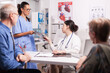 © DC Studio - Nurse with glasses giving doctor x-ray during consultation of sick married pensioners in hospital office. Young medic wearing white coat and stethoscope.