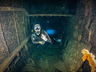 A scuba diver inside a shipwreck on the seabed shows the OK sign