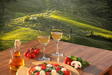 Italian pizza with glasses of white wine against Tuscan vineyards near the Florence in Italy