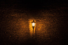 Vintage Old Street Lantern Lit With An Orange Light In Front Of A Brick Wall During A Gloomy Dark Night