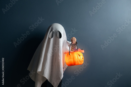 Cuadros en Lienzo A boy in ghost costume hold a pumpkin head basket with candy at the halloween night