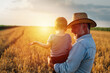 © cherryandbees - grandfather holding his grandson standing in the wheat field