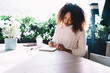 © BullRun - Young ethnic woman writing in notebook in cafe