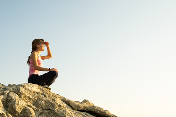 Wall Mural - Woman hiker sitting on a steep big rock enjoying warm summer day. Young female climber resting during sports activity in nature. Active recreation in nature concept.