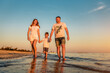 father, mother and young boy are walking at the beach