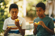 Two brothers african ethnicity sitting outdoors and tasting lemon.