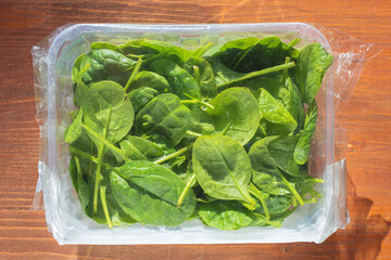 Wall Mural - fresh baby spinach in a package on wooden table