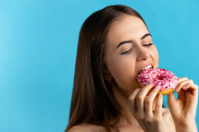 Close Up Portrait Of A Pleased Pretty Girl Eating Pink Donuts Isolated Over Blue Background