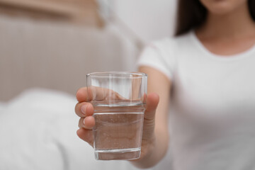 Wall Mural - Woman holding glass of water in bedroom, closeup