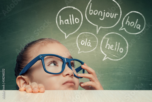 Beautiful cute little girl with eyeglasses hiding under table and looking at hello word in french, english, spanish, portuguese and german in speech balloons Canvas Print