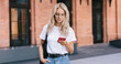 © BullRun - Attractive caucasian blonde female in eyewear reading income message on smartphone standing on urban setting background, hipster girl searching location via mobile phone application on street