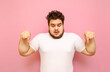© bodnarphoto - Shocked overweight guy in white t-shirt isolated on pink background, looks down and shows on copy space. Guy fat man with a beard is shocked looking down into the empty space.