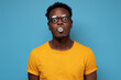 © Viktor Koldunov - Young african american man in glasses inflating ball with chewing gum while looking at camera with raised eyebrow on blue studio wall.