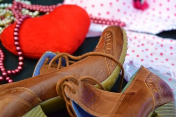 Close-up of some high-heeled shoes with a heart, pearl necklaces and a set of women's underwear in the background symbolizing the preparation of a date