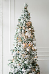 christmas tree with white, silver and gold toys on a white classic wall background
