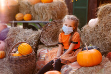 Sad Child Waiting For Halloween 2020 During Coronavirus Pandemic. Holiday In Quarantine. Protective Medical Face Mask. Social Distance Is The New Normality. Carnival Girl Dressed A Pumpkin. Masquerade