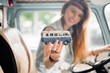 © Михаил Решетников - Young hippie woman driving a classic van with a toy car model in her hand. Smiling blurred girl holding a miniature minivan in the foreground. Auto travel concept.