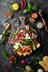 Wall Mural - A plate with cheese, salami, prosciutto and snacks on a black stone plate. Antipasto. Top view. Italian food. Free space for your text.