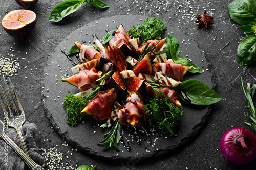 Figs with prosciutto and blue cheese and basil on a black stone plate. Food. Top view. Free space for your text.