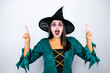 © Irene - Woman wearing witch costume over isolated white background amazed and surprised looking at the camera and pointing up with fingers and raised arms
