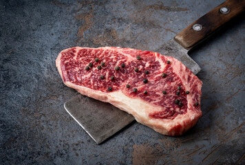 Wall Mural - Juicy Raw new strip steak and a butcher's hatchet close up on a dark background