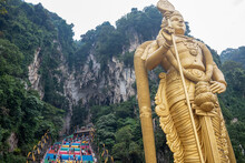 The Tall Golden Hindu Statue Of Murugan In Front Of The 272 Steps To The Batu Caves With Temples And Shrines, Near Kuala Lumpur, Malaysia
