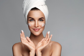 Close up of happy half naked woman applying anti age wrinkle serum, moisturizing lifting nourishing day cream on flawless skin, looking at camera, isolated on studio grey background. Beauty routine