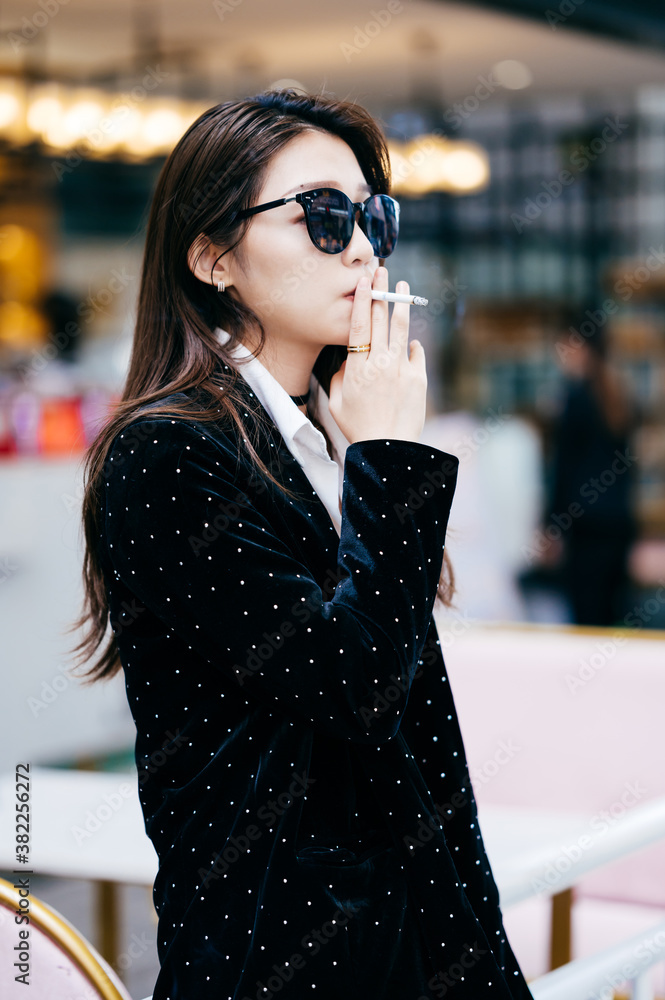 Portrait of a beautiful and fashionable young woman smoking a cigarette ...