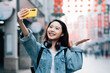© MaaHoo Studio/Stocksy - Young asian woman traveling in a city downtown and taking selfie with cell phone