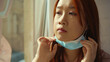 © america_stock - At sunlight asian woman remove medical mask at home sitting on windowsill and looking at street on quarantine COVID-19 pandemic epidemic depressed portrait slow motion