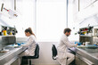 © Inuk Studio/Stocksy - Side view of man and woman in lab coats sitting at tables and examining samples while working in research laboratory together.