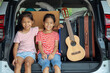 © pingpao - Happy asian child girl playing guitar and singing a song with her sister in a car trunk in family trip.