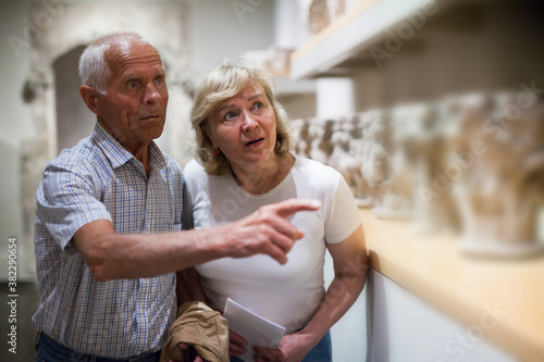 Positive elderly couple looking at exhibits on exposition of museum