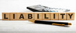 The word LIABILITY is written on the wooden cutouts between the calculator and the pen on a light background.