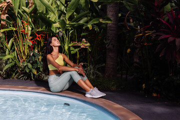  Outdoor portraif of fit slim sporty tanned pretty caucasian woman in sport yellow top and leggings on tropical background, sunny day, bright light.  