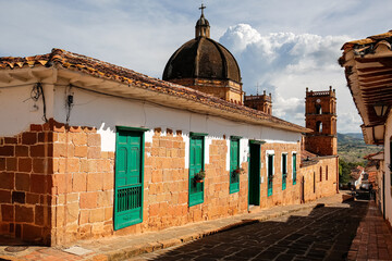 Wall Mural - Close up view to a street with typical traditional houses and cathedral in historic town Barichara on a sunny day, Colombia